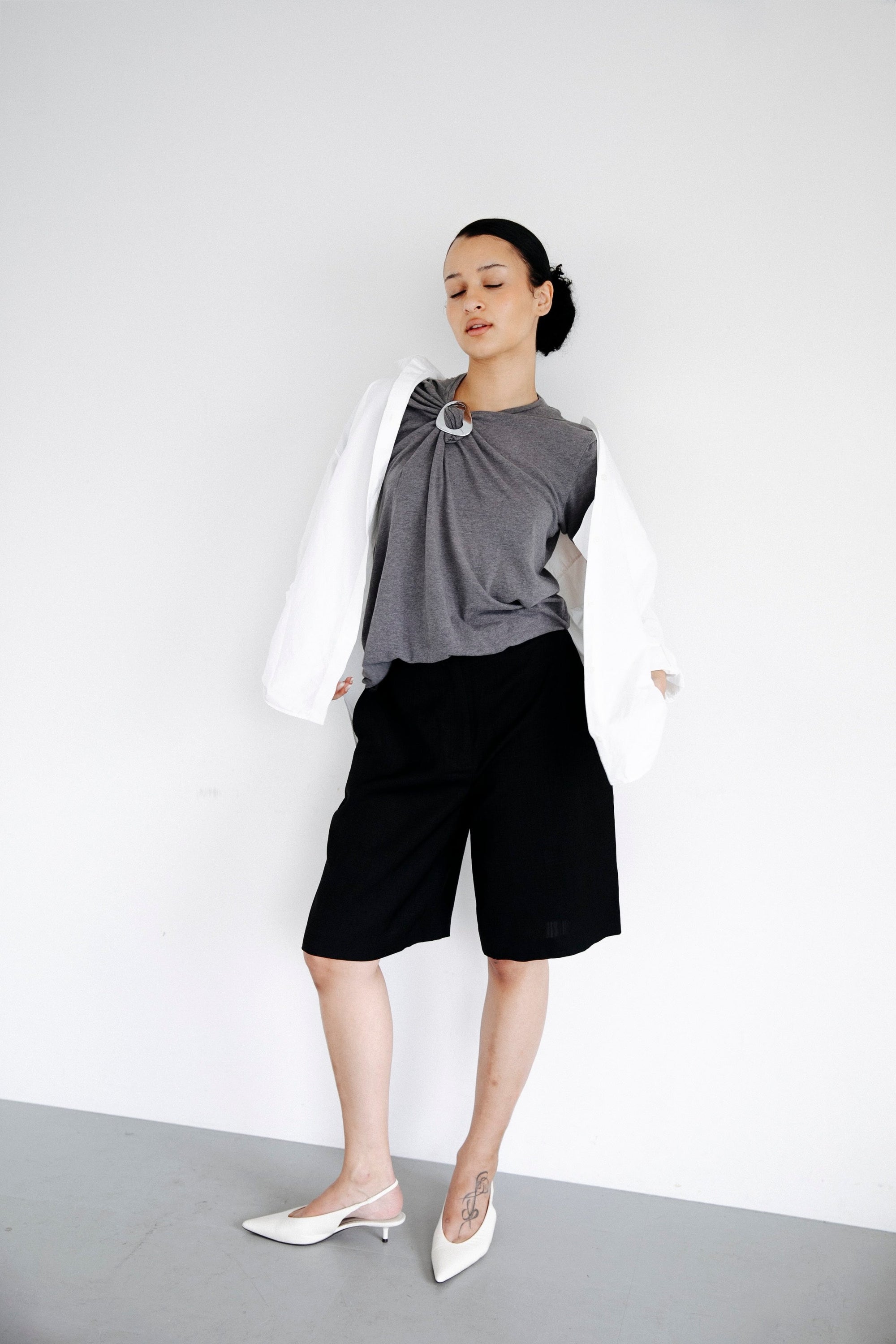 Full-body shot of a dark-haired woman in a gray draped top, white pinstripe shirt, and black wide-leg shorts, styled with MagniClip Glossy Sterling.