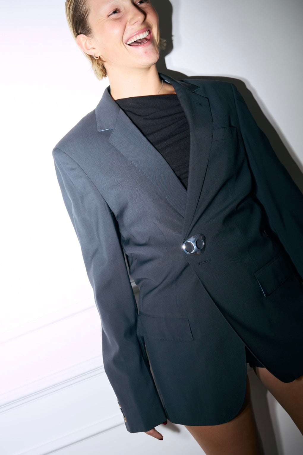 A smiling woman wearing a tailored, dark grey blazer and a black top, featuring Kitdo's MiniMagni Glossy Sterling
